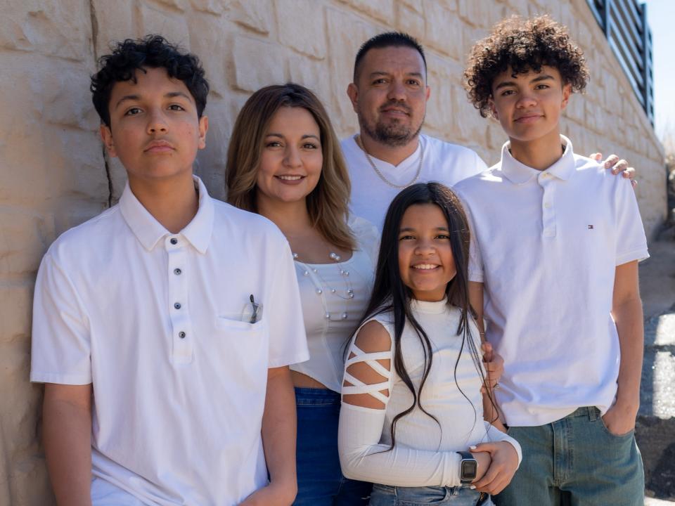 The Quinones family, all wearing white, standing against a wall.