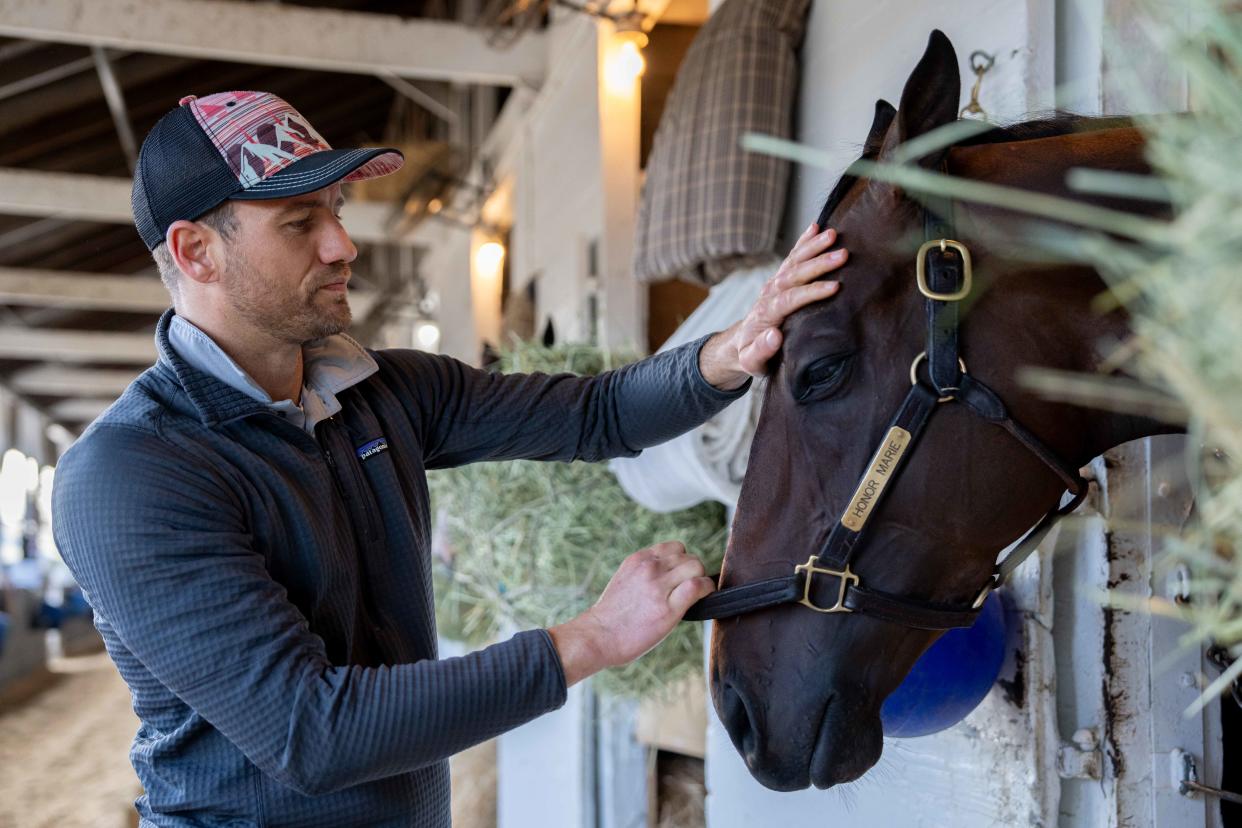 Trainer Whit Beckman pets Honor Marie in his barn April 17.