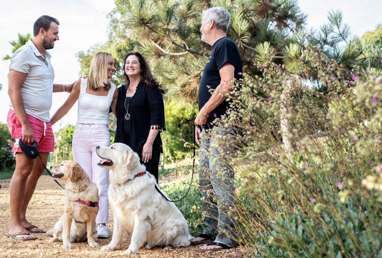 Four people sit with two dogs in a park.