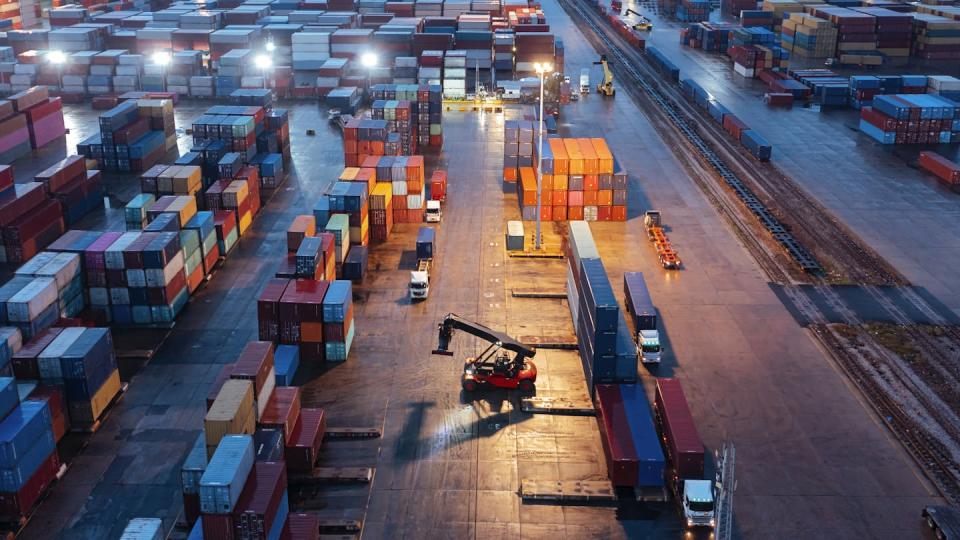 An overhead view of a container park, with a forklift truck driving between the rows of large containers.