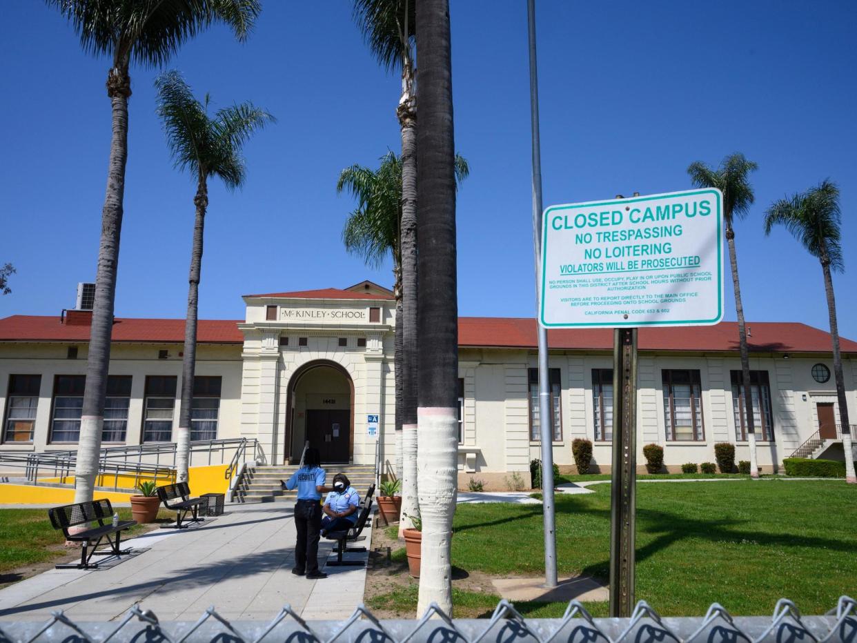 Two security guards talk on the campus of the closed McKinley School, part of the Los Angeles Unified School District (LAUSD) system, in Compton, California, just south of Los Angeles: (2020 Getty Images)