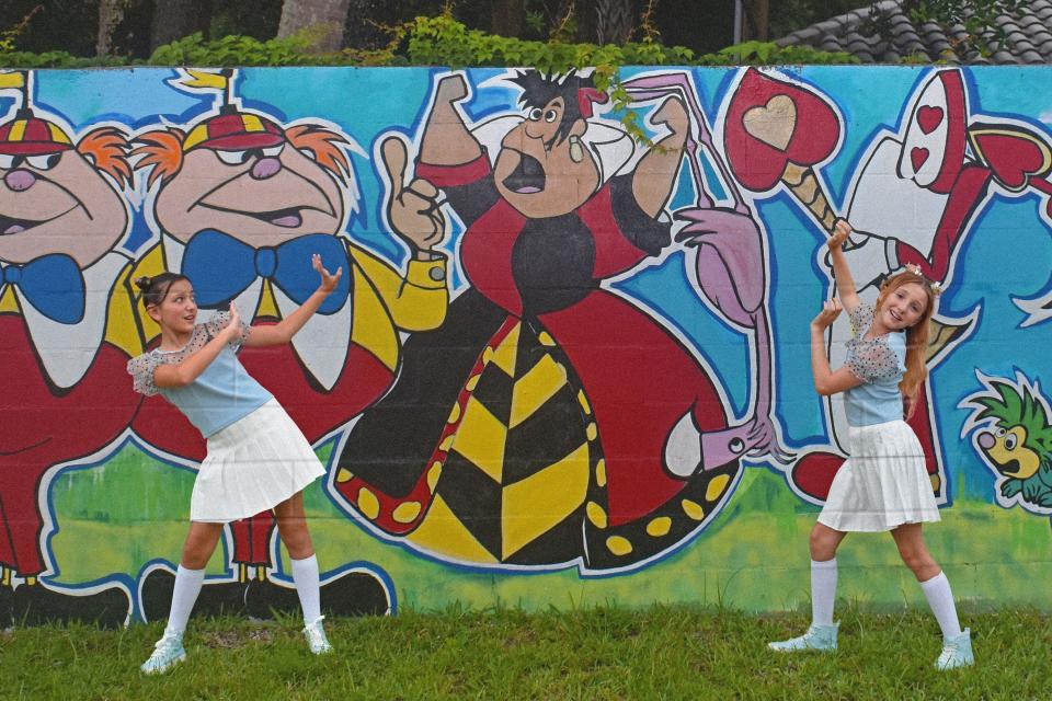 Lauralai Gant and Teagan Hascall, who play Alice in Viera Studio for the Performing Arts’ production “Y2K Alice in Wonderland," pose in front of a mural by artist Jen Gallo.