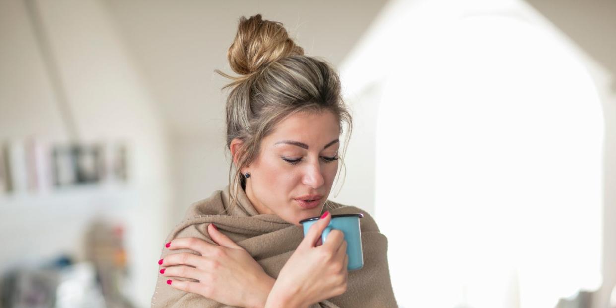 woman wrapped having drink while standing at home