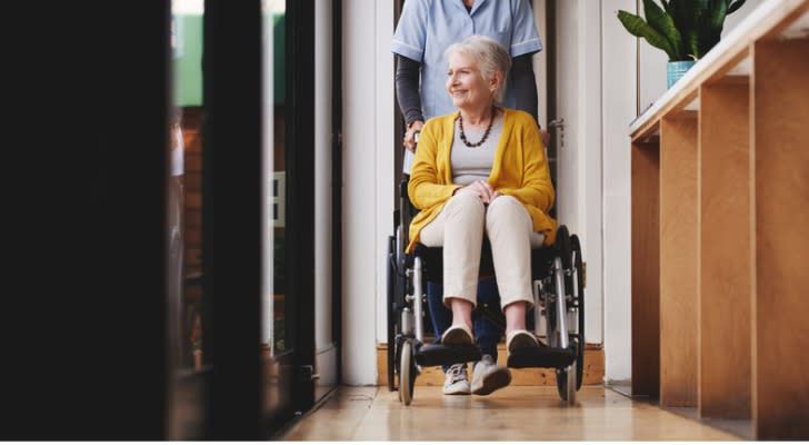 A nursing home patient is escorted out of her room from an employee. 