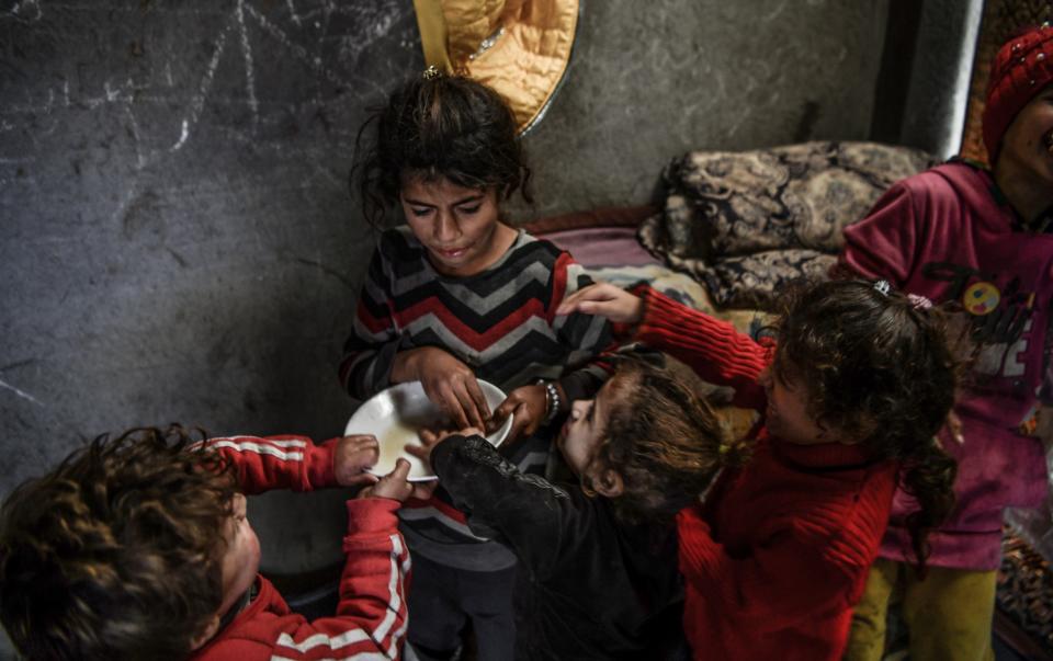 Palestinian children try to eat from a single bowl inside the tent