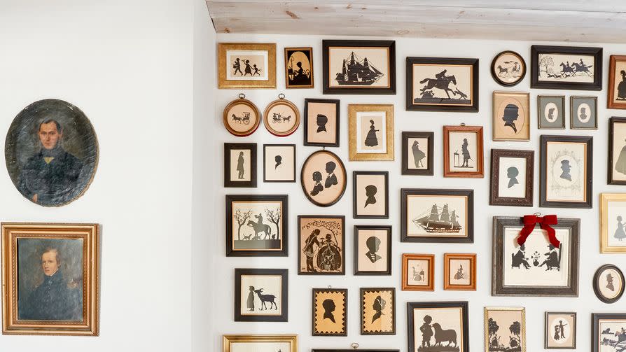 2nd floor stairwell banister with citrus garland in front of gallery wall entirely covered with antique silhouettes in 216 year old dutch colonial farmhouse in hortonville, new york, owned by shawn lang and kristofer prepelica