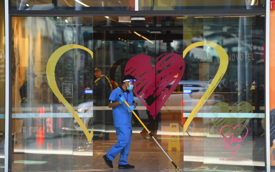 A worker wearing PPE mops the floor at the entrance to a quarantine hotel in Melbourne - JAMES ROSS/EPA-EFE/Shutterstock