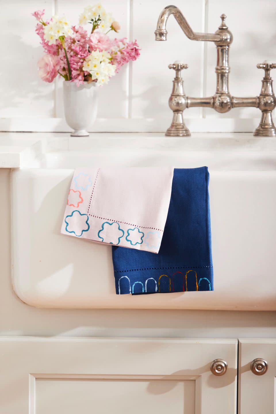 printed dishtowels hung over a farm sink with a bouquet of pink flowers on the counter