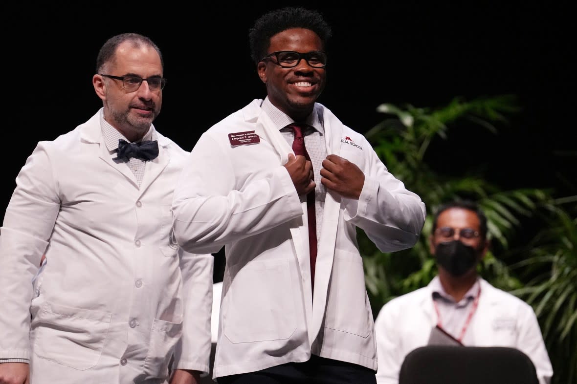 MINNEAPOLIS, MN. - AUGUST 2022: Medical student Benjamin Owens smiles as he gets his white coat from Dr. Nersi Nikakhtar during the University of Minnesota Medical Schools annual White Coat Ceremony for the class of 2026 Friday, Aug. 19, 2022 at the Northrop Memorial Auditorium on the University campus in Minneapolis. The Class of 2026 on the Twin Cities Campus includes 167 students with half of them Black, Indigenous and people of color. (Photo by Anthony Souffle/Star Tribune via Getty Images)