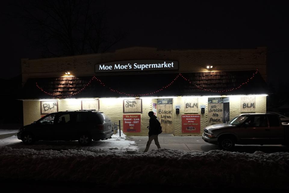 A person walks past a boarded-up grocery store, Monday, Jan. 4, 2021, in Kenosha, Wis. Kenosha Police Officer Rusten Sheskey opened fire on Jacob Blake in August after responding to a domestic dispute, leaving him paralyzed. The incident has sparked numerous protests. (AP Photo/Morry Gash)