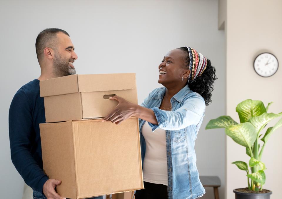 A man holding two boxes laughs with a woman at home