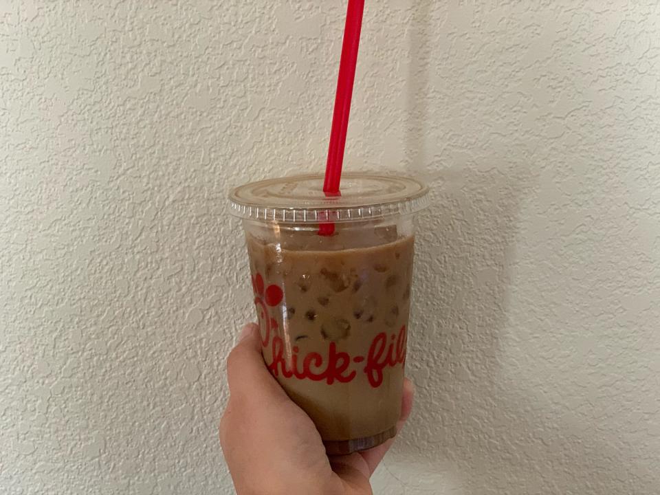 hand holding Chick-fil-a iced coffee in front of beige wall