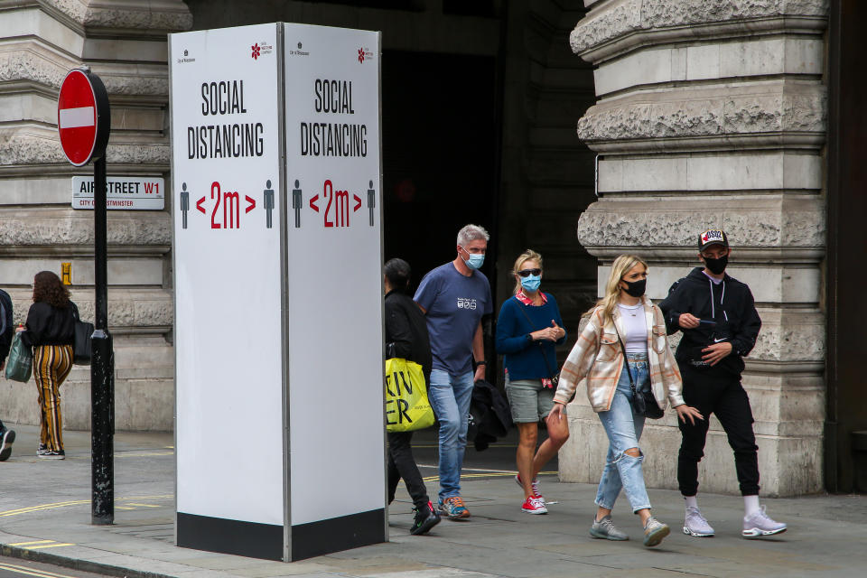 LONDON, UNITED KINGDOM - 2020/08/31: Members of public wearing face masks walk past a "Social Distancing" sign at Regents Street during coronavirus pandemic. It is mandatory to wear face masks while travelling. (Photo by Dinendra Haria/SOPA Images/LightRocket via Getty Images)