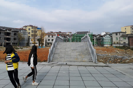Teenage girls walk past a bridge and buildings under construction in Rucheng county, Hunan province, China December 3, 2018. Picture taken December 3, 2018. REUTERS/Shu Zhang