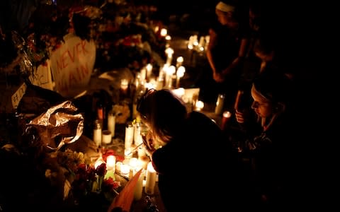 People light candles in front of mementoes placed in front of the fence of the Marjory Stoneman Douglas High School  - Credit: CARLOS GARCIA RAWLINS/Reuters