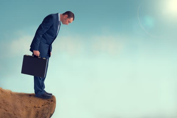 Man wearing a suit and holding a briefcase, looking over a cliff.