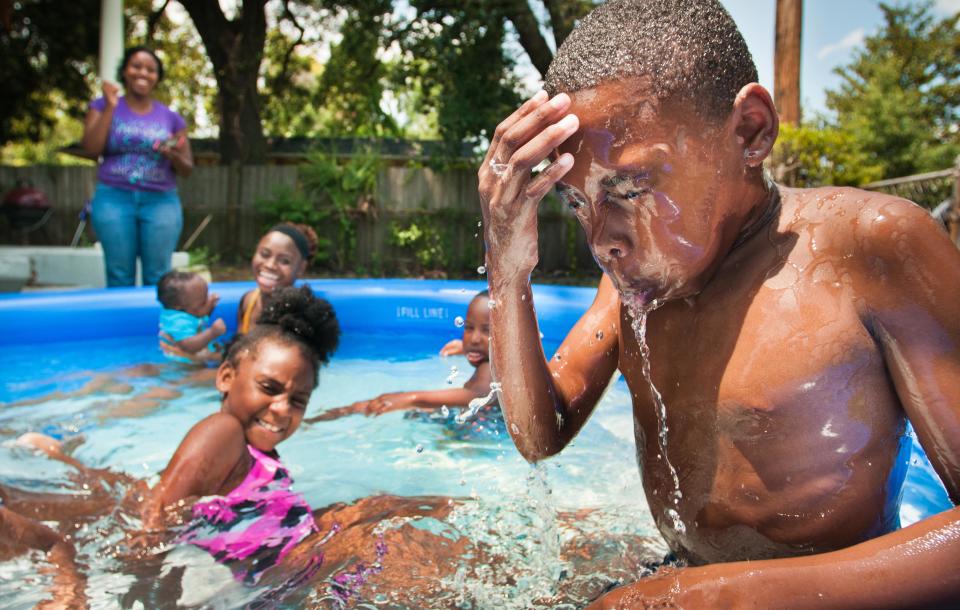 Summer heat drove kids in this August 2011 photo to cool off in a front yard pol at a home off East 12th Street, an area that was redlined in the 1930s.