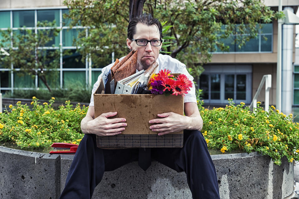 Photo of an out-of-work businessman, sitting outside his office building with his box of meager belongings as he gets rained on.  