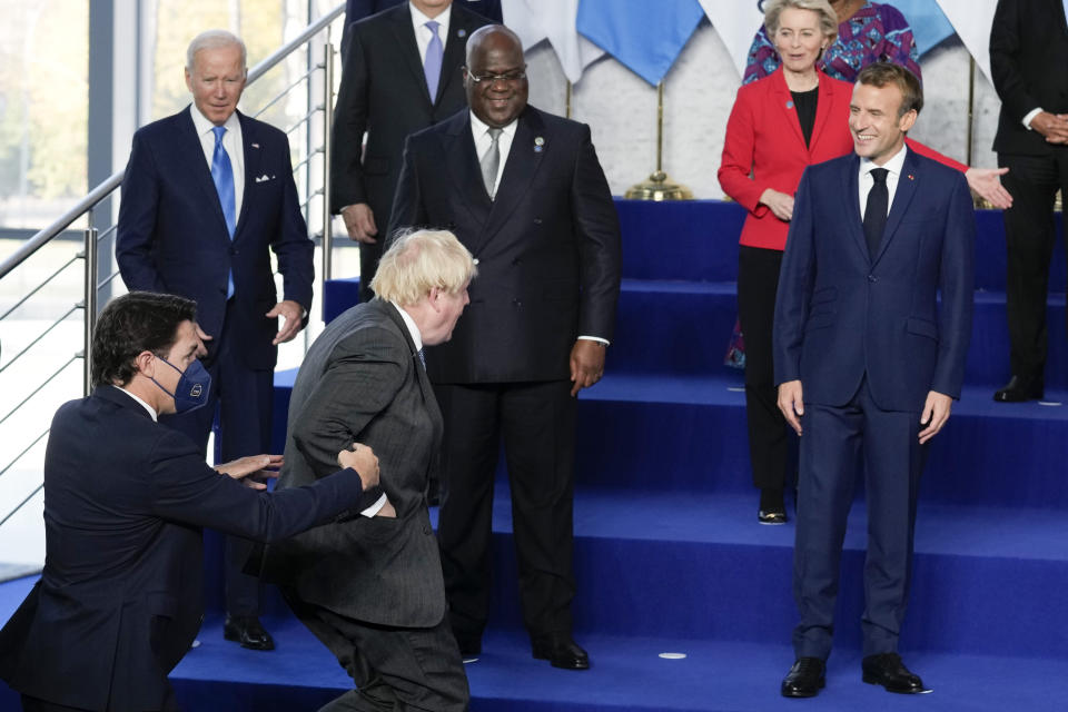 French President Emmanuel Macron laughs as British Prime Minister Boris Johnson, center, is helped up the stage as he arrives late for the group photo of world leaders at the La Nuvola conference center for the G20 summit in Rome, Saturday, Oct. 30, 2021. The two-day Group of 20 summit is the first in-person gathering of leaders of the world's biggest economies since the COVID-19 pandemic started. (AP Photo/Kirsty Wigglesworth, Pool)