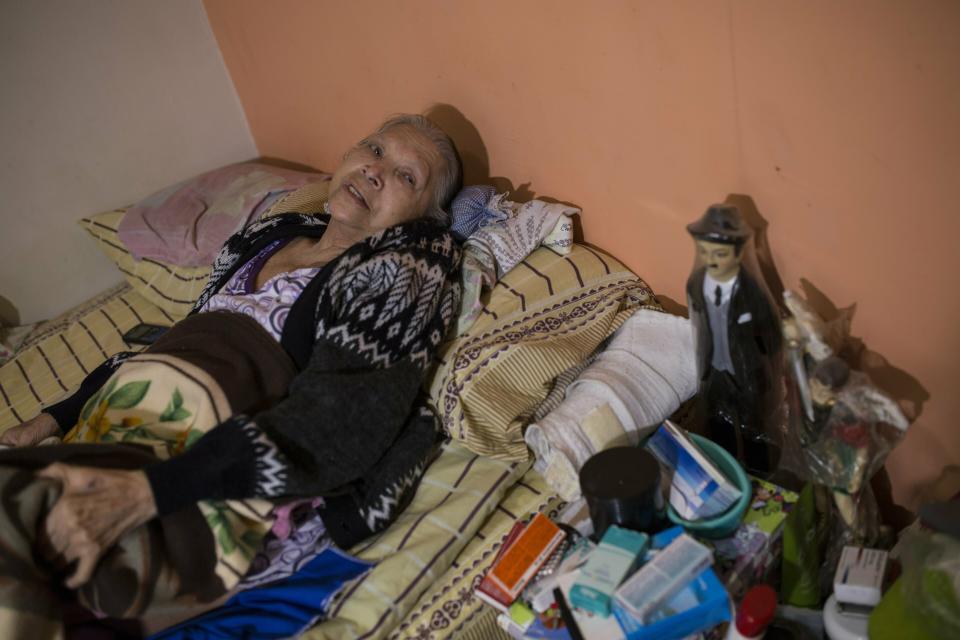 In this Feb. 4, 2019 photo, diabetes patient Aminta Villamizar lies on her bed next to a statue of Dr. Jose Greogrio Hernandez, a 19th century Venezuelan doctor who treated the poor and is revered throughout the country as a saint, in Caracas, Venezuela. “I was a person who worked my entire life, but this sickness destroyed me,” she said, complaining of joint pain and blurry vision. “If we don’t receive help, we’ll have to resign ourselves to God’s will.” (AP Photo/Rodrigo Abd)