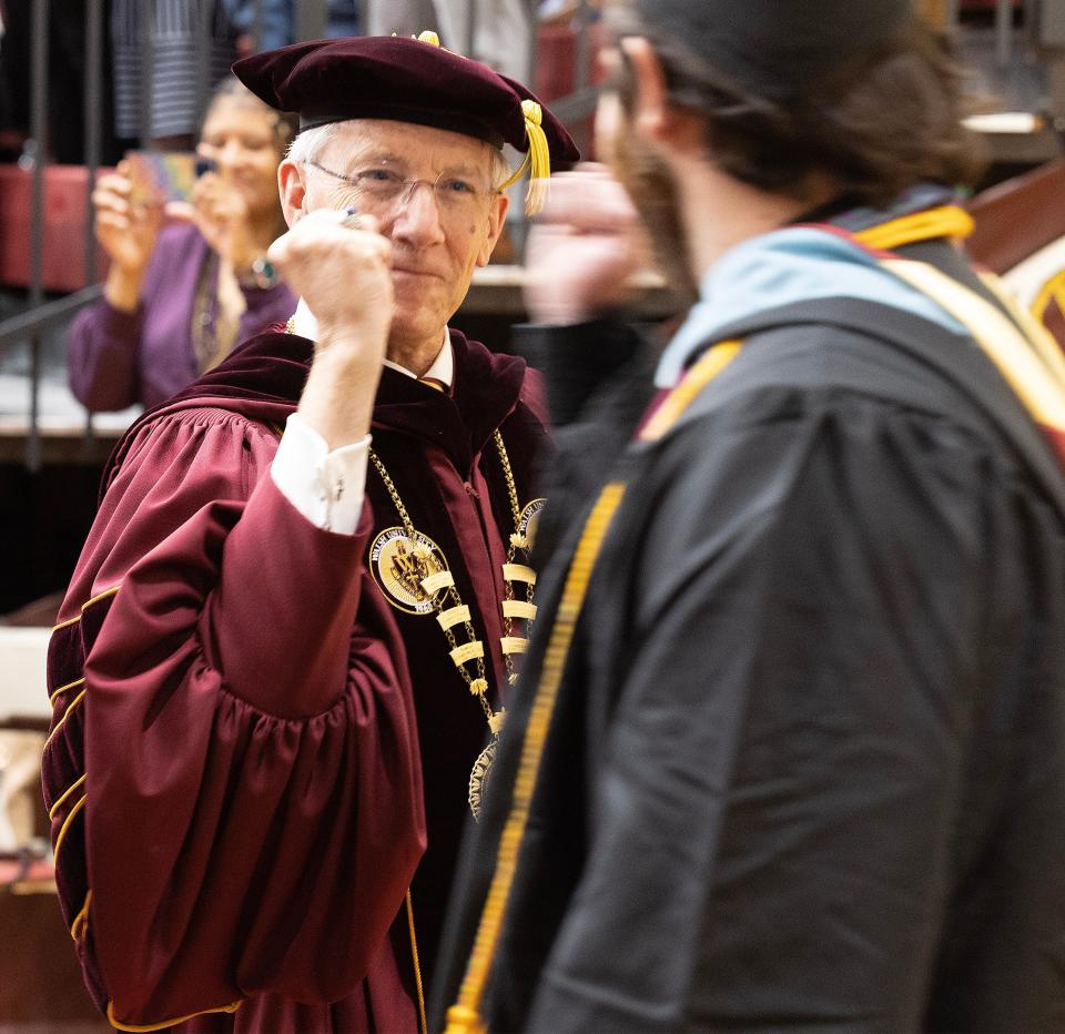 Walsh University President Tim Collins fist-bumps graduates as they file in for commencement at the university in North Canton on Saturday.