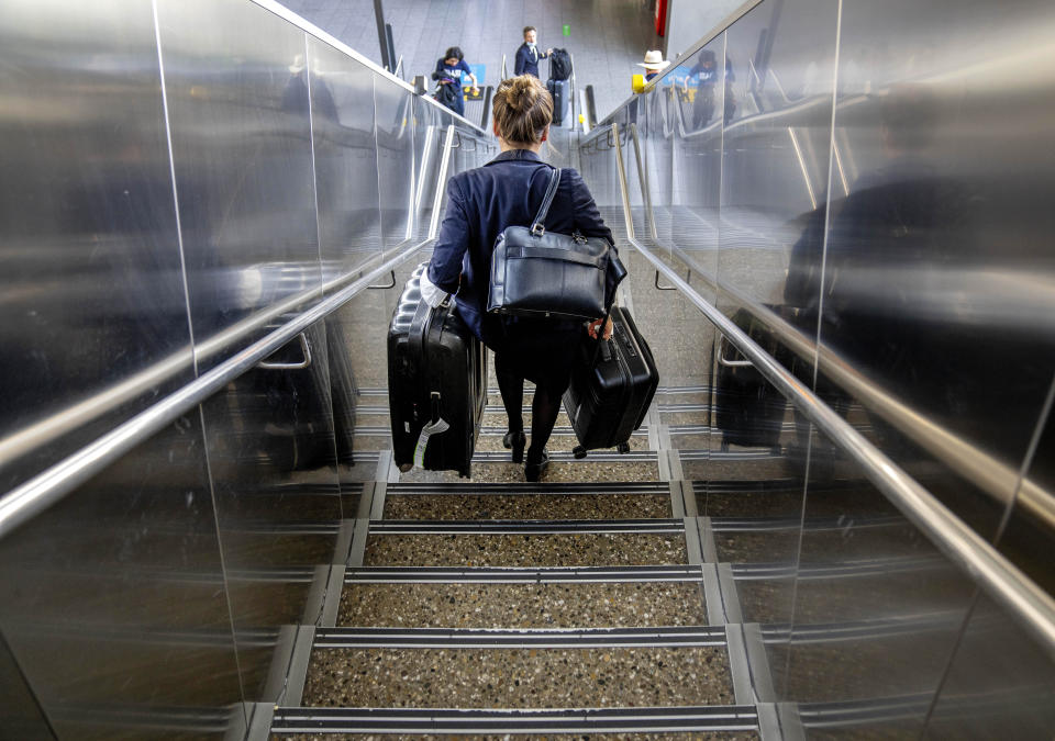 FILE - A woman carries her luggage down the stairs at the international airport in Frankfurt, Germany, Tuesday, June 21, 2022. (AP Photo/Michael Probst, File)