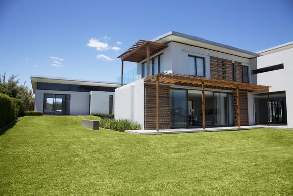 A two-story house, white with wood accents, and an L-shaped lawn on a clear day.