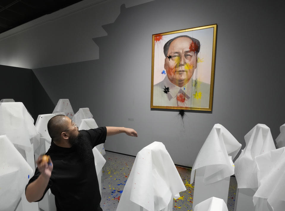Chinese dissident artist Badiucao throws paintballs at an image of Mao Zedong in a performance for reporters ahead of the opening of a new exhibition in Warsaw, Poland on Friday, June 16, 2023. The museum faced demands from the Chinese embassy not to open the exhibition, "Tell China's Story Well," which is highly critical of China's human rights record. (AP Photo/Czarek Sokolowski)