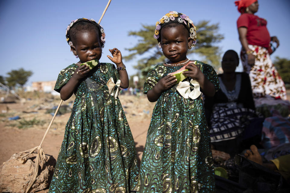 Twins eat slices of watermelon Thursday Nov. 25, 2021 at the Patte d'Oie district of Ouagadougou, Burkina Faso, where mothers of twins come to beg on the road. In Burkina Faso, a country with a strong belief in the supernatural, twins are regarded as children of spirits whose mothers were specially selected to bear them. (AP Photo/Sophie Garcia)