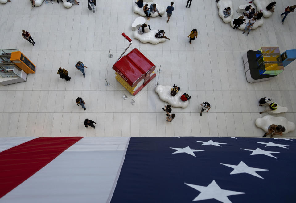 People walk under a flag in the Oculus transportation hub Wednesday, Sept. 11, 2019, in New York. From Europe to Japan, President Donald Trump has stirred up under-the-radar trade disputes that potentially could erupt within weeks or months with damaging consequences. (AP Photo/Craig Ruttle)