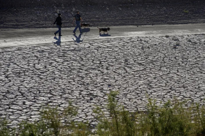 FILE - People walk by cracked earth in an area once under the water of Lake Mead at the Lake Mead National Recreation Area, Jan. 27, 2023, near Boulder City, Nev. The intensity of extreme drought and rainfall has “sharply” increased over the past 20 years, according to a study published Monday, March 13, 2023, in the journal Nature Water. (AP Photo/John Locher, File)