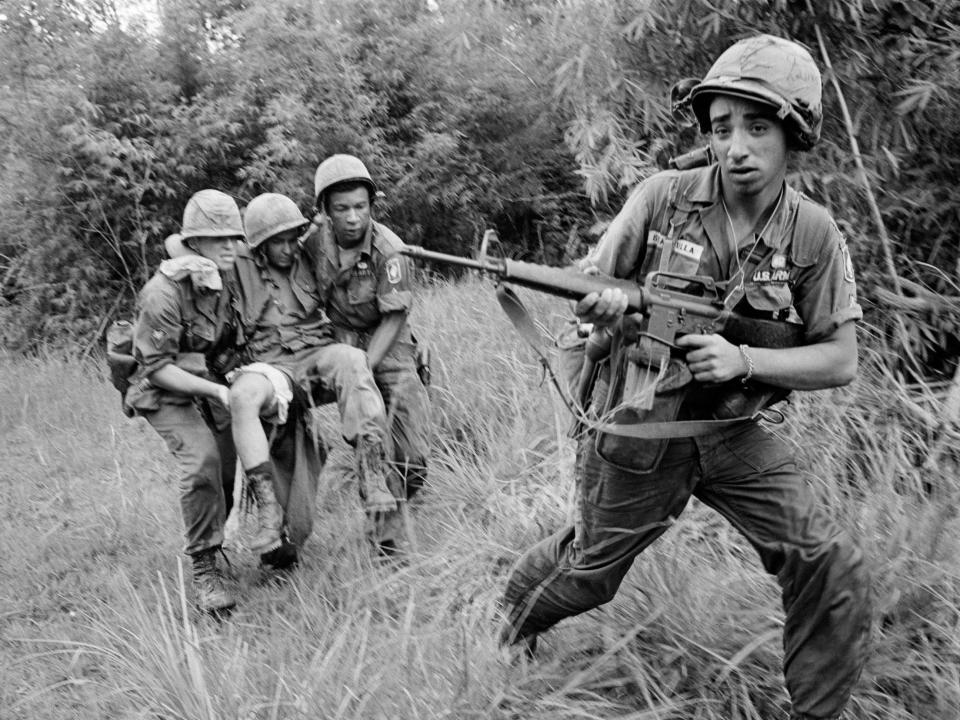 Paratroopers carry a wounded soldier while another holds an M16 in Vietnam in 1965.
