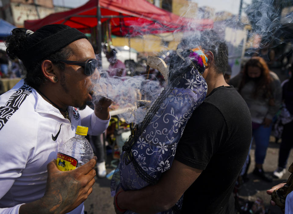 José Luis Candanosa sopla humo de cigarro sobre "La Santa Muerte", por la creencia de que éste la puede purificar, en el barrio de Tepito de la Ciudad de México, el martes 1 de noviembre de 2022. La Santa Muerte es una imagen de culto y un santo popular, una personificación de la muerte, asociada con la curación, la protección y la entrega segura al más allá por parte de sus devotos. (AP Foto/Fernando Llano)