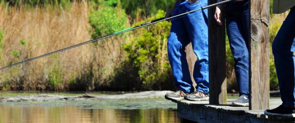 Three fishermen stand on a wooden dock over a lake.  They are bream fishing.  Photo shows only their legs and shoes.