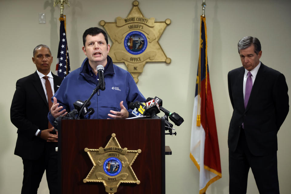 Spokesperson for Duke Energy Corporation Jeff Brooks, center, speaks on Monday, Dec. 5, 2022, at a news conference about an attack on critical infrastructure that has caused a power outage to many around Moore County at the Moore County Sheriff's Office in Carthage, N.C. North Carolina Gov. Roy Cooper is at right and Secretary of N.C. Department of Public Safety Eddie M Buffaloe, stands at left. (AP Photo/Karl B DeBlaker)