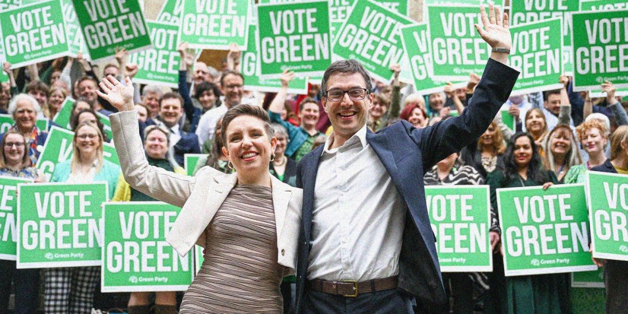 carla denyer and adrian ramsay stand in front of supporters holding signs saying vote green