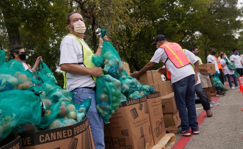 Wearing a face mask to prevent to spread of COVID-19, volunteer Scot Wingo grabs bags of food to distribute during a North Texas Food Bank drive-thru event on Oct. 22, 2020, in Dallas.