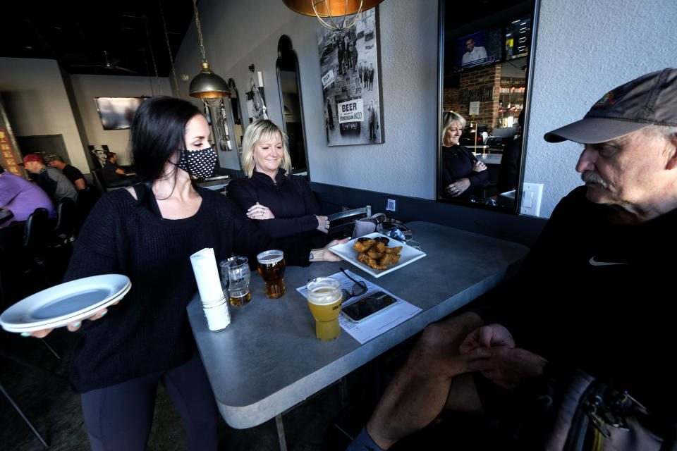 Waitress Penny Thompson, left, wearing a face mask serves Steve Zell, right, and his wife Julie at Notorious Burgers restaurant in Carlsbad, Calif., on Friday, Dec. 18, 2020. (AP Photo/Ringo H.W. Chiu)