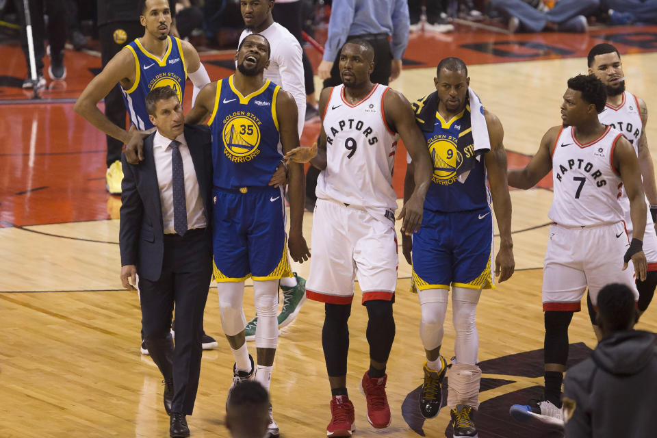 FILE - In this Monday, June 10, 2019 file photo, Golden State Warriors forward Kevin Durant (35) walks off the court after sustaining an injury as he is accompanied by Toronto Raptors center Serge Ibaka (9) and Warriors forward Andre Iguodala (9) and guard Kyle Lowry (7) during first-half basketball action in Game 5 of the NBA Finals in Toronto. On Friday, June 14, 2019, The Associated Press found that a video circulating on the internet that appeared to show fans in a Toronto bar cheering as Durant’s injury is shown on a large TV screen was deceptively altered, with the Durant injury image inserted into unrelated footage of cheering soccer fans. (Chris Young/The Canadian Press via AP)