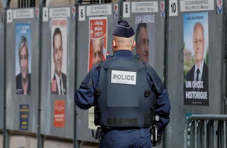 A policeman walks by election posters near a polling station during the first round of 2017 French presidential election in Paris, France, April 23, 2017. REUTERS/Christian Hartmann