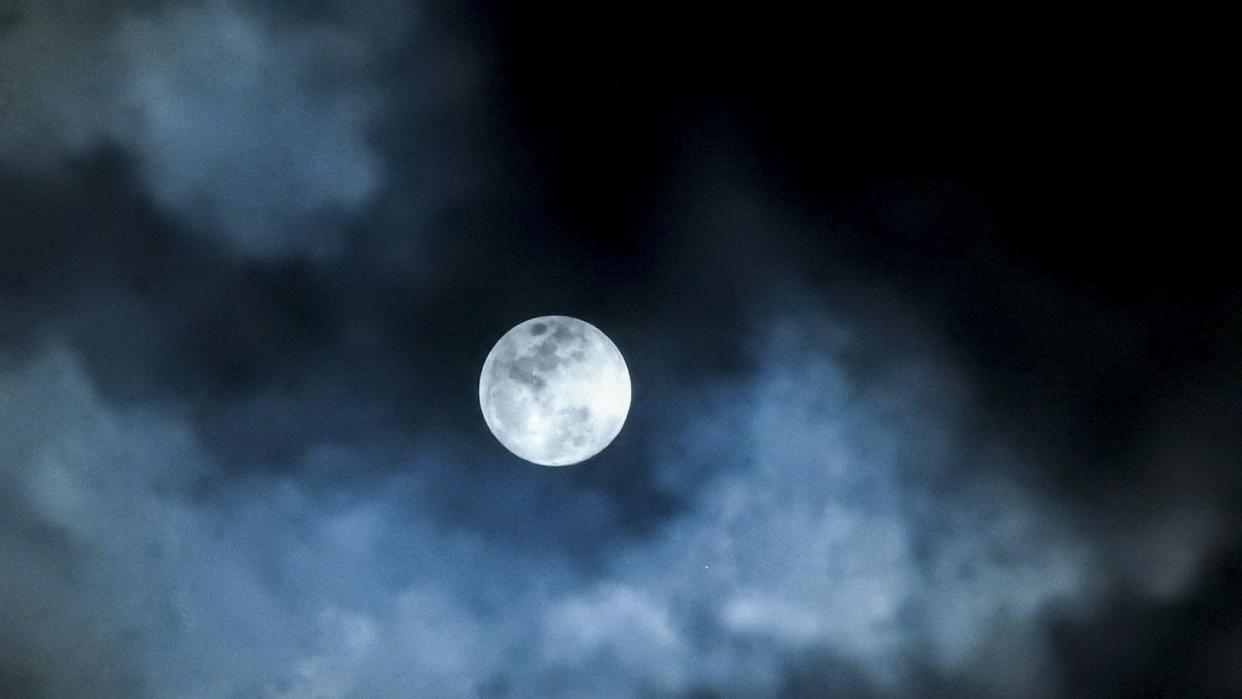 Close up detail of a full moon shining through bluish clouds