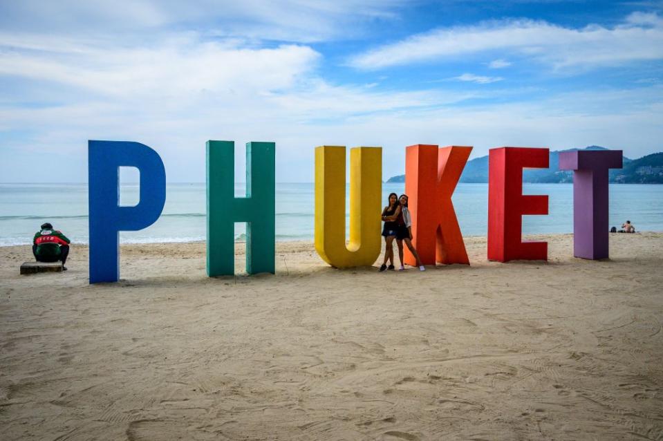 Women pose for a photo in front of a sign at Patong Beach on the Thai island of Phuket on October 28, 2021, as the country prepares to welcome visitors fully vaccinated against the Covid-19 coronavirus without quarantine from November 1.<span class="copyright">MLADEN ANTONOV/AFP via Getty Images</span>