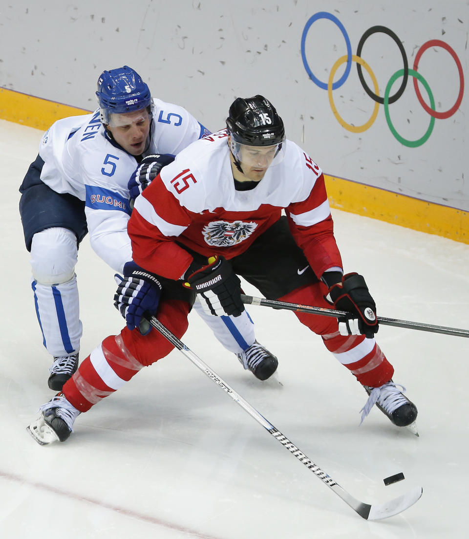 Finland defenseman Lasse Kukkonen reaches for he puck against Austria forward Manuel Latusa in the second period of a men's ice hockey game at the 2014 Winter Olympics, Thursday, Feb. 13, 2014, in Sochi, Russia. (AP Photo/Mark Humphrey)