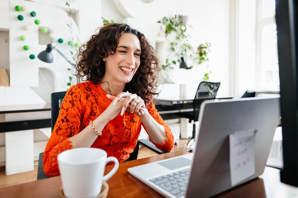 A transgender woman smiling while video calling a business partner using her laptop at the office.