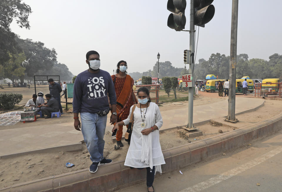 Tourists wear masks to save themselves from pollution as they cross a road in New Delhi, India, Tuesday, Nov. 12, 2019. A thick haze of polluted air is hanging over India's capital, with authorities trying to tackle the problem by sprinkling water to settle dust and banning some construction. The air quality index exceeded 400, about eight times the recommended maximum. (AP Photo/Manish Swarup)