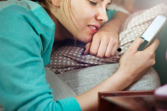 A young woman lying in bed holding her smartphone