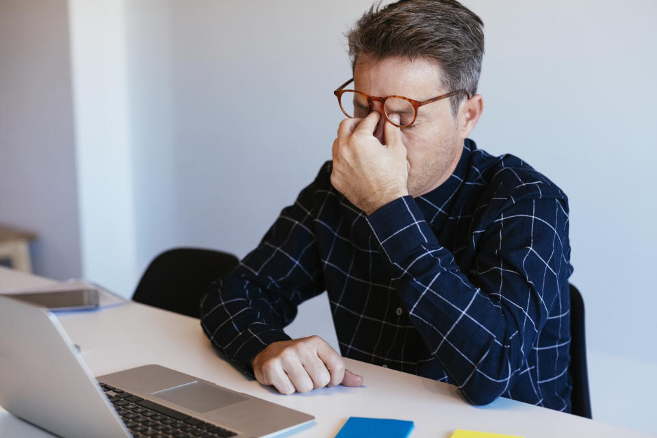 A man sits in front of a computer and rubs his eyes.