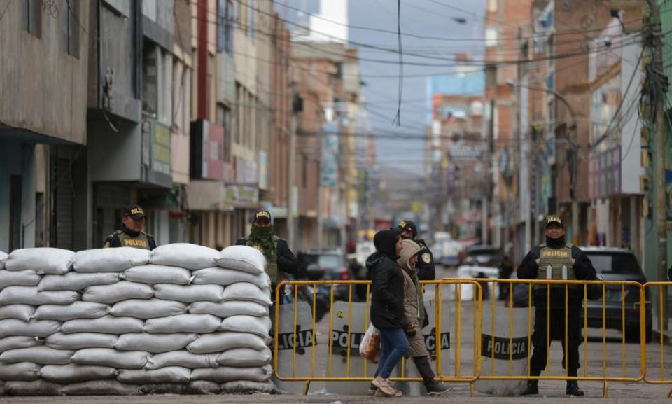 People walk past a police barricade on a street. Protests and roadblocks in Peru’s southern Andes have recently hardened.