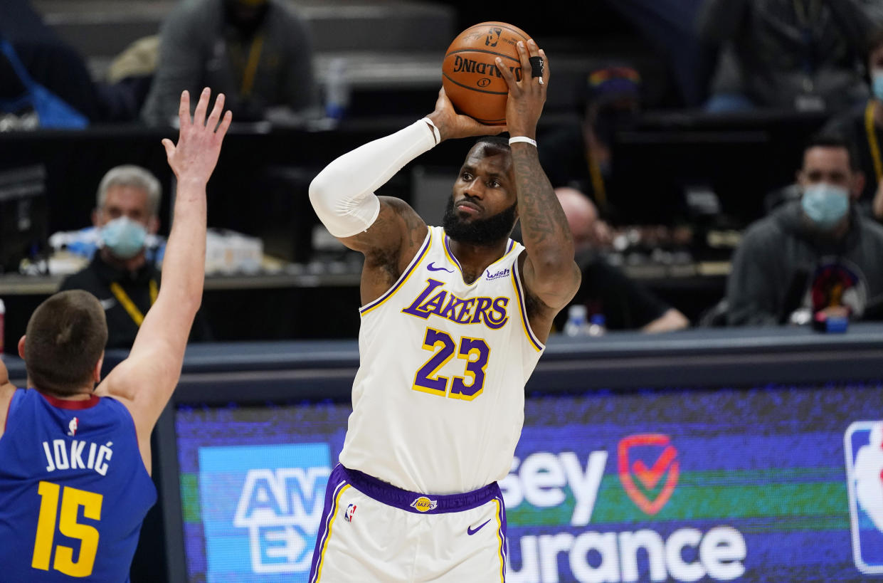 LeBron James with the ball in his hands in a shooting motion above his head as Nikola Jokic holds up a hand to defend in front.