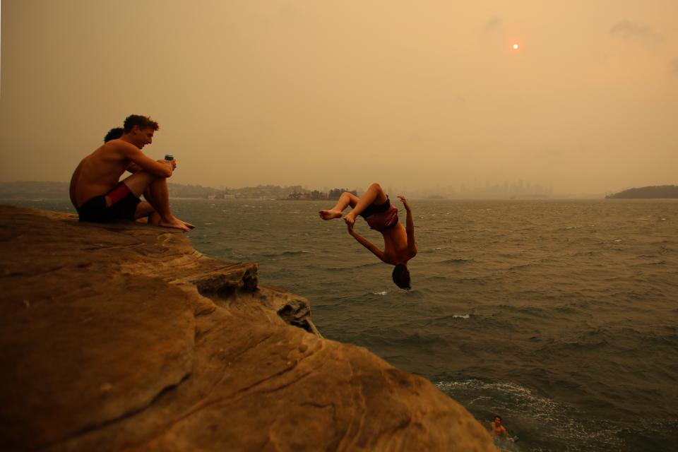 Smoke haze from bushfires blankets the Sydney CBD as beachgoers Jump from a cliff in Nielsen Park.